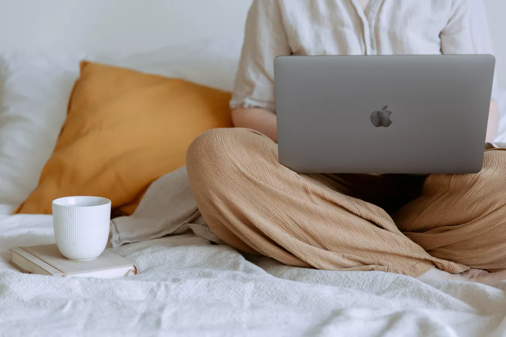 A woman sitting on a bed with a laptop.