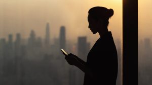 A silhouette of a woman using a tablet in front of a city.