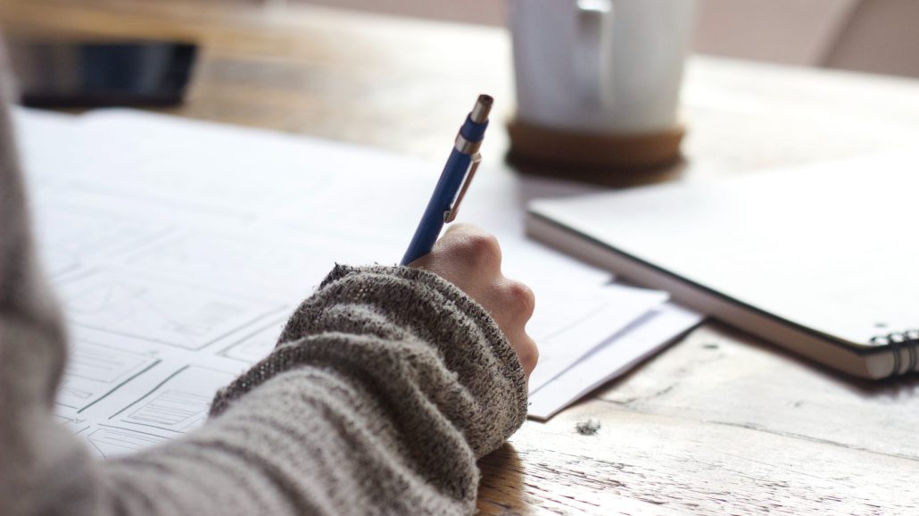 A person writing on a piece of paper at a desk.